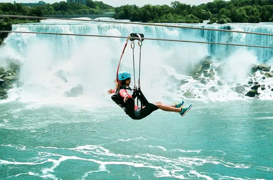 A lady on a Zipline across a beautiful scenic waterfall and vast green green land with Trees